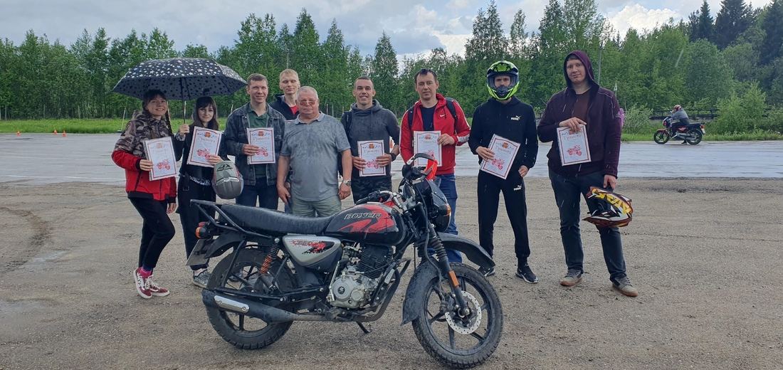 Выпускники автошколы с грамотами под дождём у мотоцикла