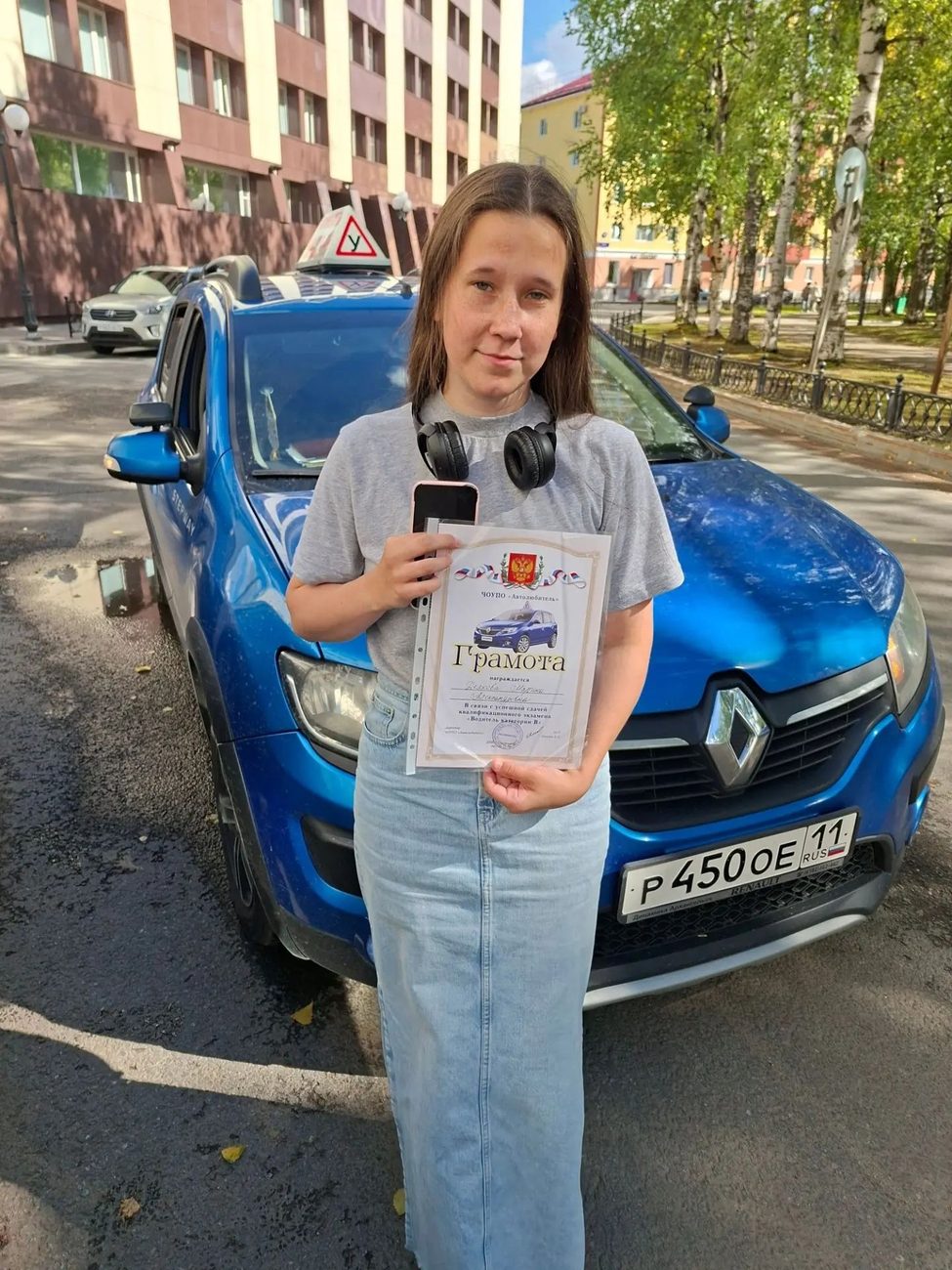 Выпускница автошколы со свидетельством у синего учебного Renault Sandero с буквой У на крыше