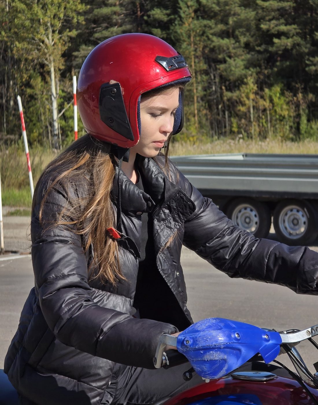 Ученица в красном шлеме на учебном мотоцикле на автодроме автошколы
